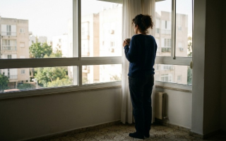 אישה עומדת ליד חלון ומביטה החוצה עם כוס קפה - חרדה ופחד בטיפול הומאופתי